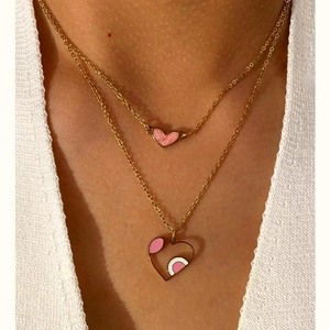 Detail view of layered gold heart necklaces with pink enamel pendant on model neck
