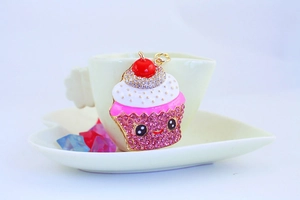 Detail of cute cupcake keychain with pink rhinestones hanging on a white coffee cup