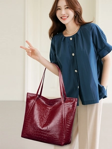 Detailed view of red crocodile pattern tote bag held by a model in casual office attire