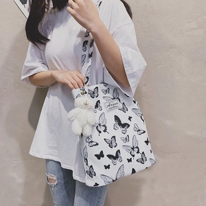 Close-up of white canvas tote bag with black butterfly prints and plush bear charm