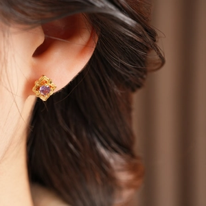 Close-up of vintage gold floral earring with purple gemstone on model's ear