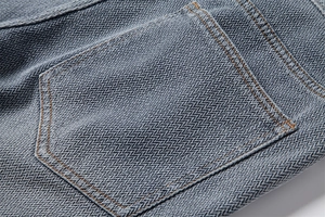 Detailed close-up of blue denim fabric showing herringbone texture and reinforced back pocket