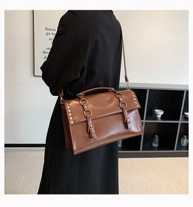 Detail view of vintage brown PU leather messenger bag with buckle straps and rivet details