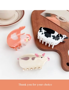 Three animal-shaped acetate hair claws including cow and pig designs on a wooden tray