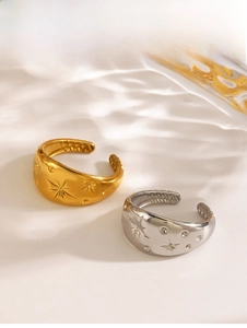Detail of star-engraved gold and silver open rings with crystal accents on a wavy glass surface