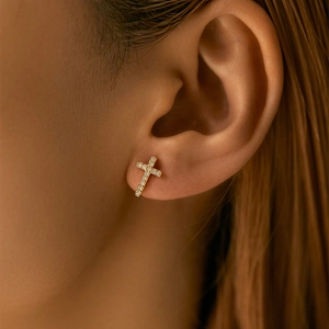 Close-up of a minimalist 18K gold-plated cross stud earring with zircon on an ear