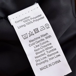 Detail of white laundry care label on 100% polyester fabric showing washing symbols