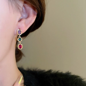 Detail of colorful oval zircon earrings with purple, green, and red stones on gold base