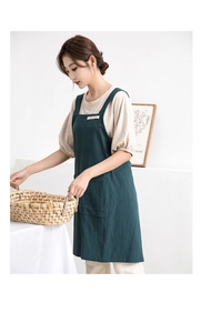 Detail of dark green cotton linen apron featuring front pockets in a bright indoor setting