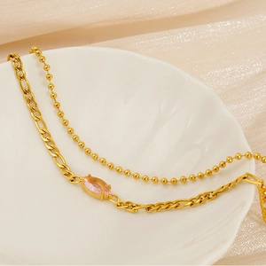 Close-up of double-layer gold chain with pink marquise zircon on a white shell tray