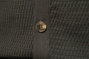 Detail of waffle-knit fabric and amber resin button on men's dark green cardigan