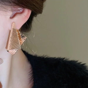 Detail of irregular golden metal earring with textured hammered and striped finish on ear