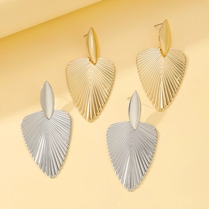 Golden and silver palm leaf stud earrings with detailed radial texture on a beige background