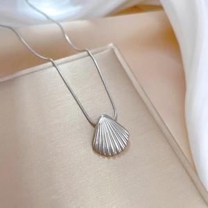 Macro shot of silver shell pendant on fine chain over golden brushed texture background