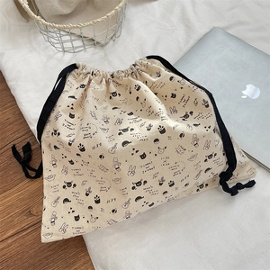 Detail of cute cat printed drawstring canvas bag on white fabric near a silver laptop
