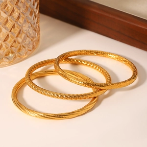 Close-up of three gold hollow textured stainless steel bangles with spiral and dot patterns