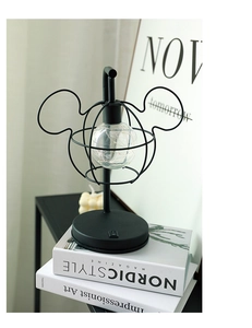 Detail view of a black metal Mickey mouse shaped lamp with a glass bulb on a desk