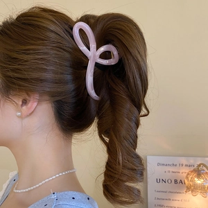 Detail view of a light pink bow-shaped hair claw clip styling a high ponytail hairstyle