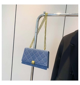 Close-up of blue denim crossbody bag with quilted pattern and gold chain strap on a hanger