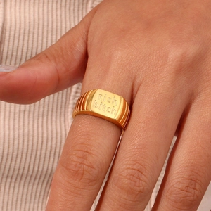 Makroaufnahme des vergoldeten Metallrings mit Rich Bitch Buchstaben-Gravur im Detail
