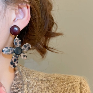 Close-up of leopard print flower drop earrings with red studs on a model in knitwear