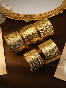 Detailansicht goldener Manschettenknöpfe mit floralen Mustern und Mandala-Gravuren