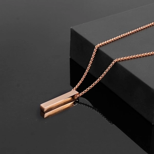 Detail of a rose gold square vertical bar necklace on a glossy black surface