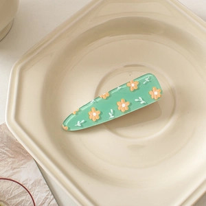 Close-up of a light green acrylic duckbill hair clip with yellow flower patterns