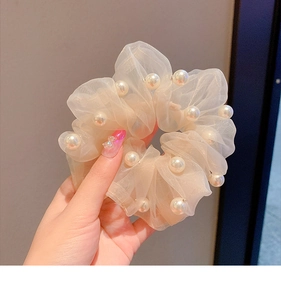 Detail of champagne organza scrunchie with elegant pearl accents in soft light