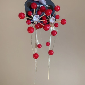 Macro shot of red bead cluster earrings with golden tassels and silver needles
