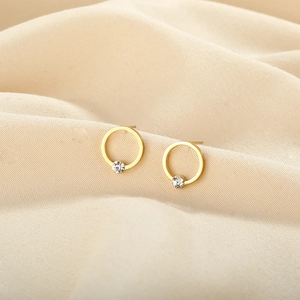 Macro detail of gold-plated hoop earrings featuring a sparkling inset zircon on soft fabric