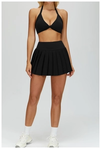 Detail of black halter yoga top with twist knot and high-waisted pleated tennis skirt