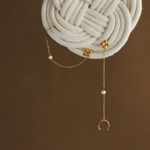 Detail of clover tassel earring with pearls and gold-plated chain on woven background