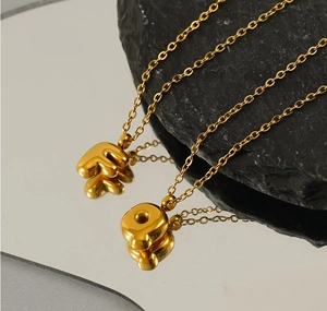 Close-up of golden bubble letters F and Q pendants on delicate stainless steel chains