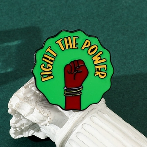 Macro detail of a green enamel Fight the Power fist brooch leaning against a white column