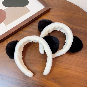 Detail showing two plush panda ear headbands in black and white on a wooden surface