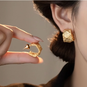 Detailed macro view of gold-tone geometric C-shaped earrings with unique hammered texture