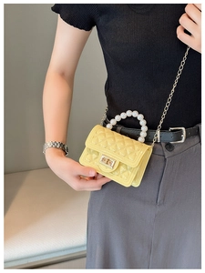 Close-up of yellow quilted mini bag with pearl handle and golden chain strap