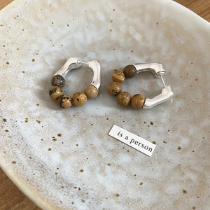 Détail macro de créoles en argent avec perles en pierre marron sur plateau céramique