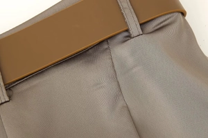 Detailed view of high-quality grey satin trousers with coffee-colored belt and silk texture