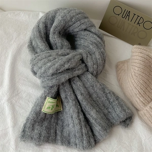 Thick grey knit wool scarf for women with green decorative label on white background