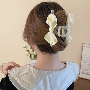 Detail of cream silk ribbon bow hair claw clip worn on a low bun hair style for women