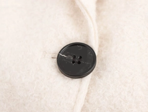Close-up of black four-hole buttons on white plush textured long wool coat fabric