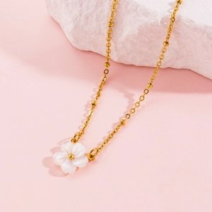 Elegant gold chain necklace with white shell flower pendant on pink decorative background