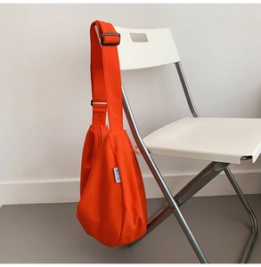 Detail of vibrant orange oxford sling bag with blue logo label on a white chair