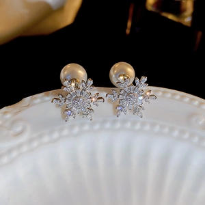 Macro shot of silver snowflake earrings with sparkling zircons and a white pearl on ceramic