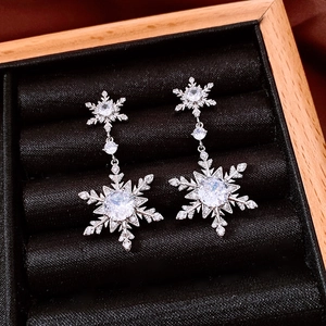 Macro shot of sparkling 18k silver needle snowflake drop earrings on black velvet