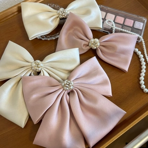 Detail of cream and pink oversized satin bow hair clips with central pearl flower accents