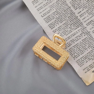 Detail of square gold metal hair claw clip with textured surface on vintage book