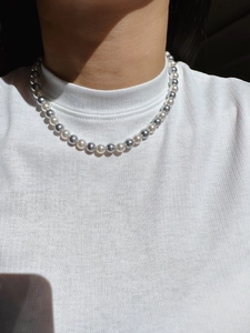 Detail of grey and white round pearl necklace layered on a white ribbed top